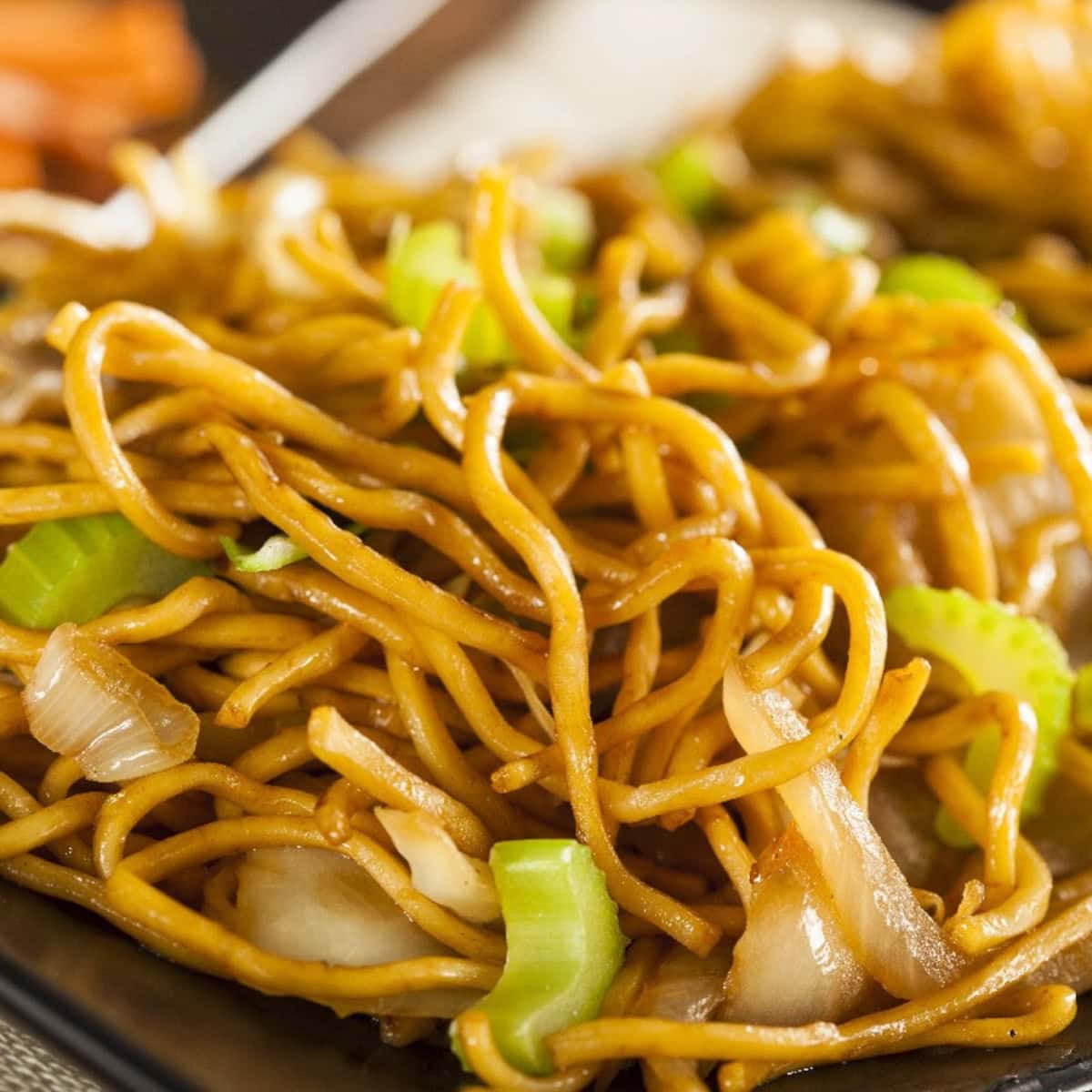 Chow mein noodles stir-fried with cabbage and celery on a black plate.