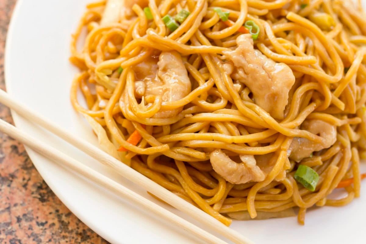 Lo mein noodles with chicken and vegetables served with chopsticks.