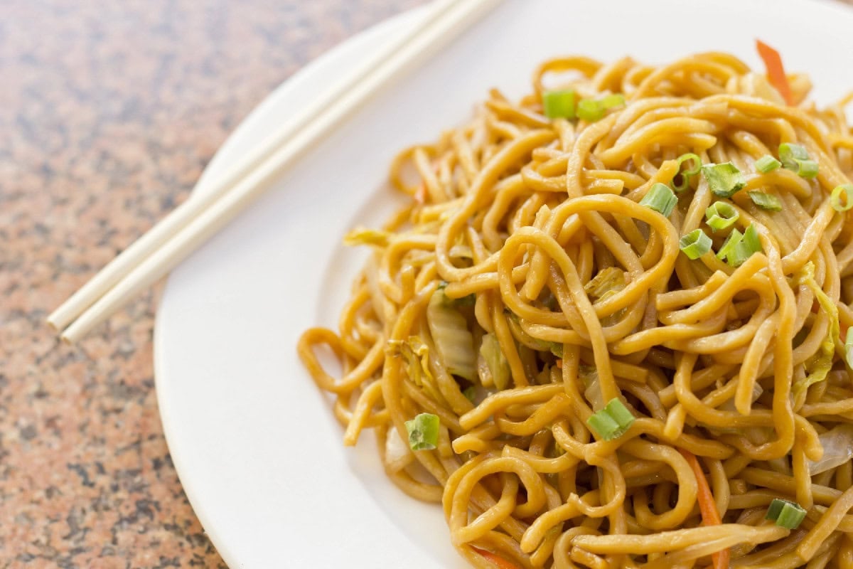 Chinese lo mein noodles garnished with green onions on a white plate.