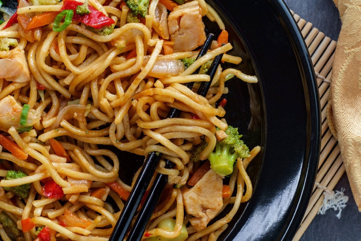 Chicken lo mein noodles with vegetables served in a black bowl.