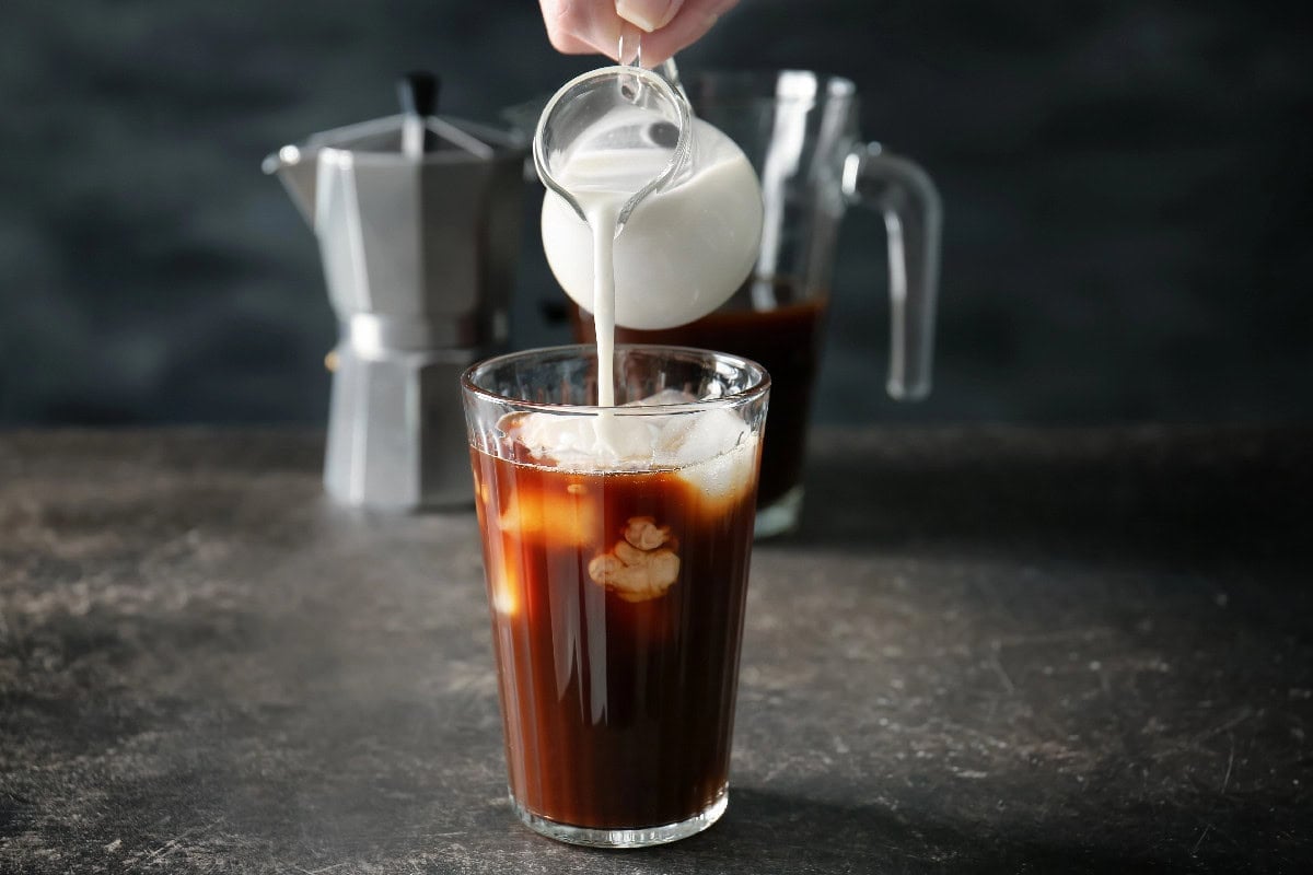 Cold brew coffee with milk being poured over ice in a glass.