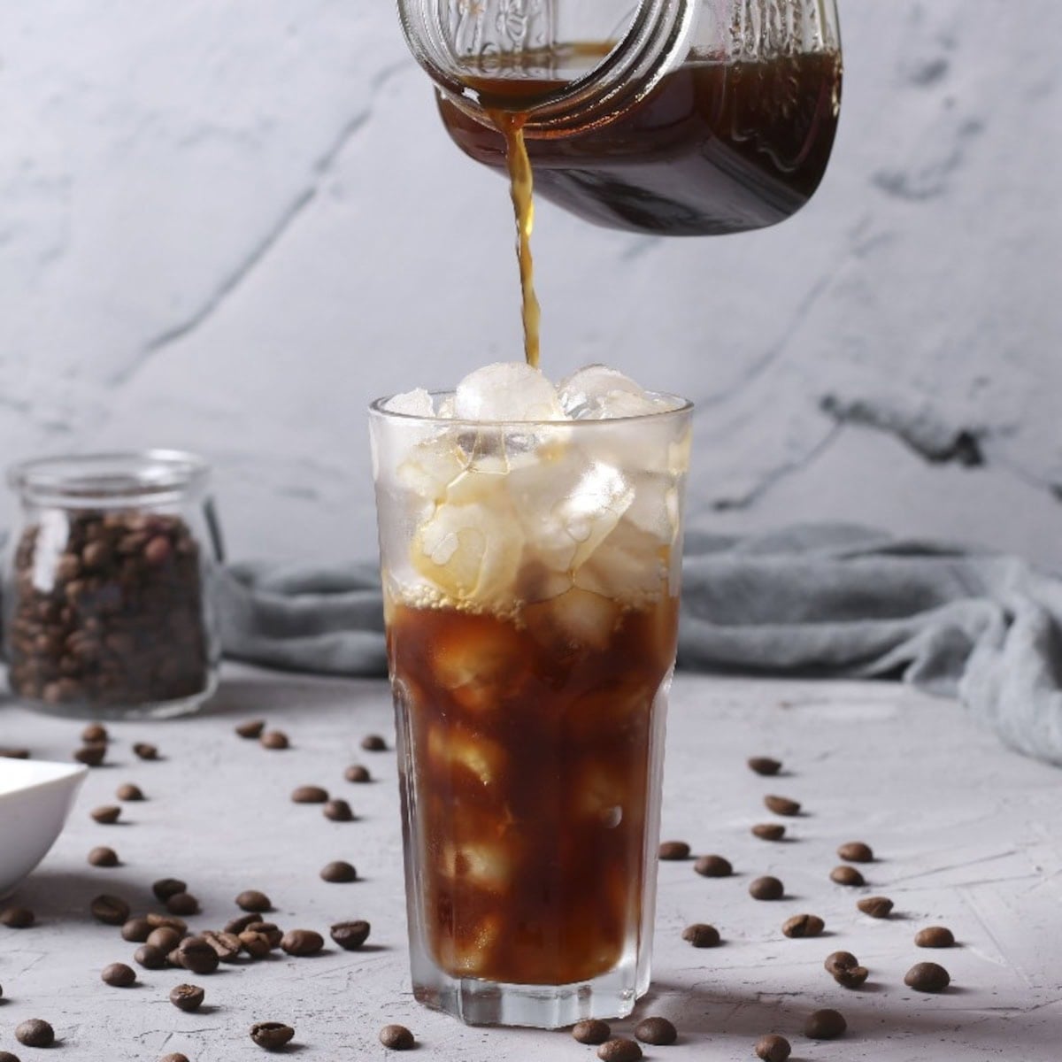 Iced cold brew coffee poured over ice with some coffee beans.