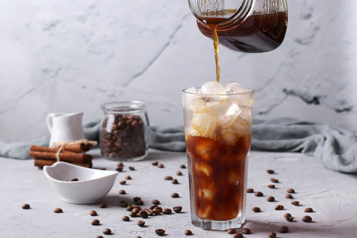 Iced cold brew coffee poured over ice with coffee beans.