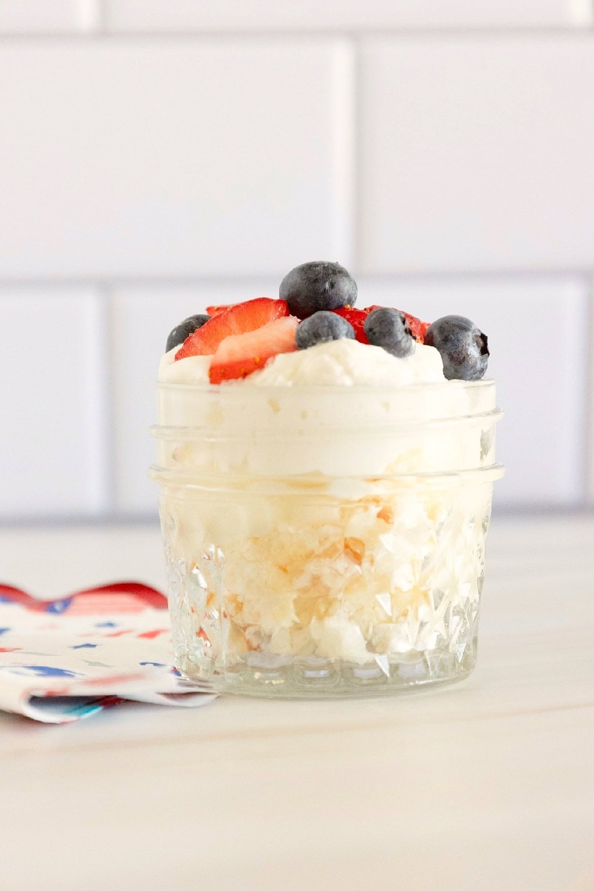 Mini red, white, and blue trifle topped with whipped topping, fresh strawberries, and blueberries in a decorative glass dish.