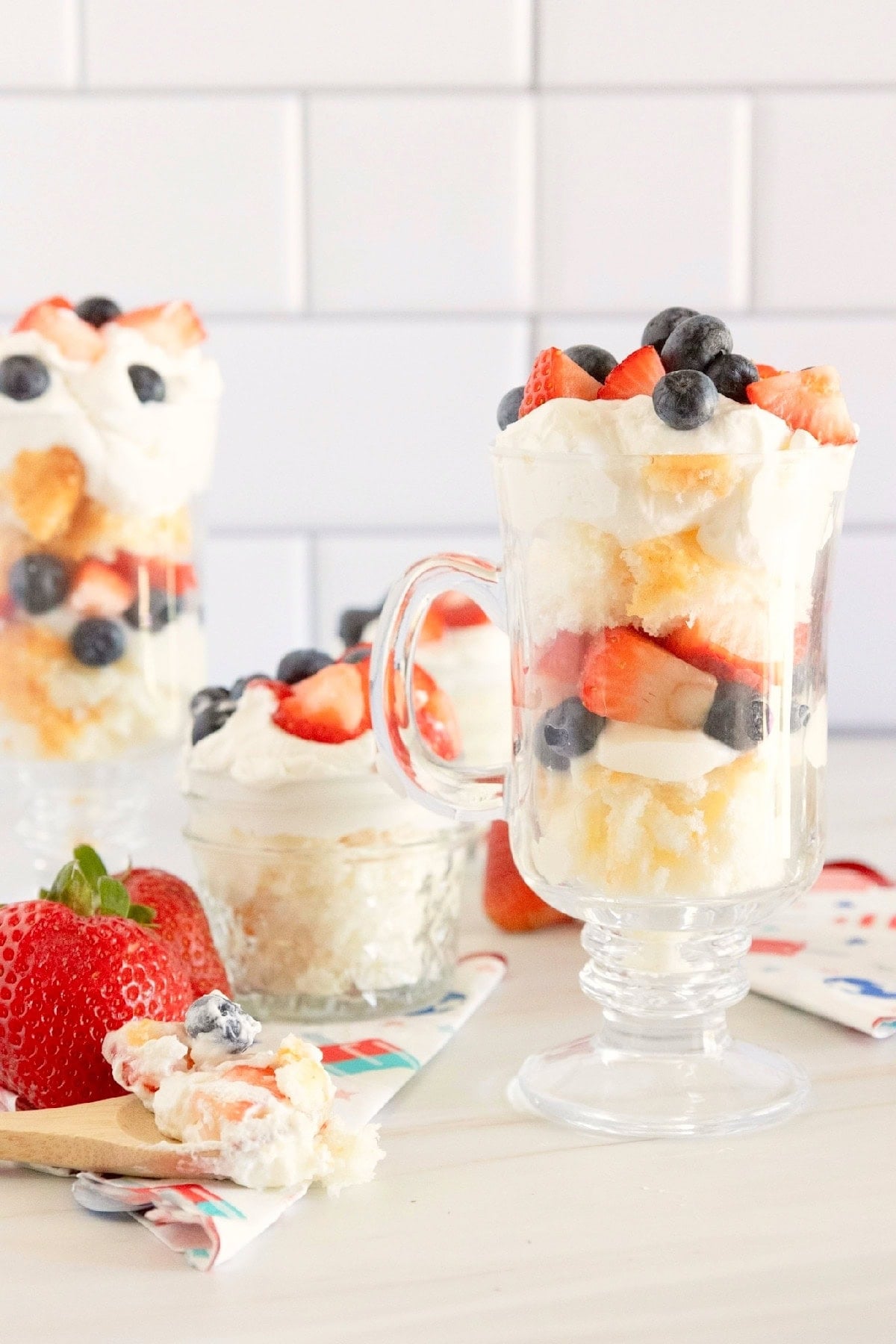 Red, white, and blue trifle desserts arranged on a table with fresh strawberries and patriotic napkins.