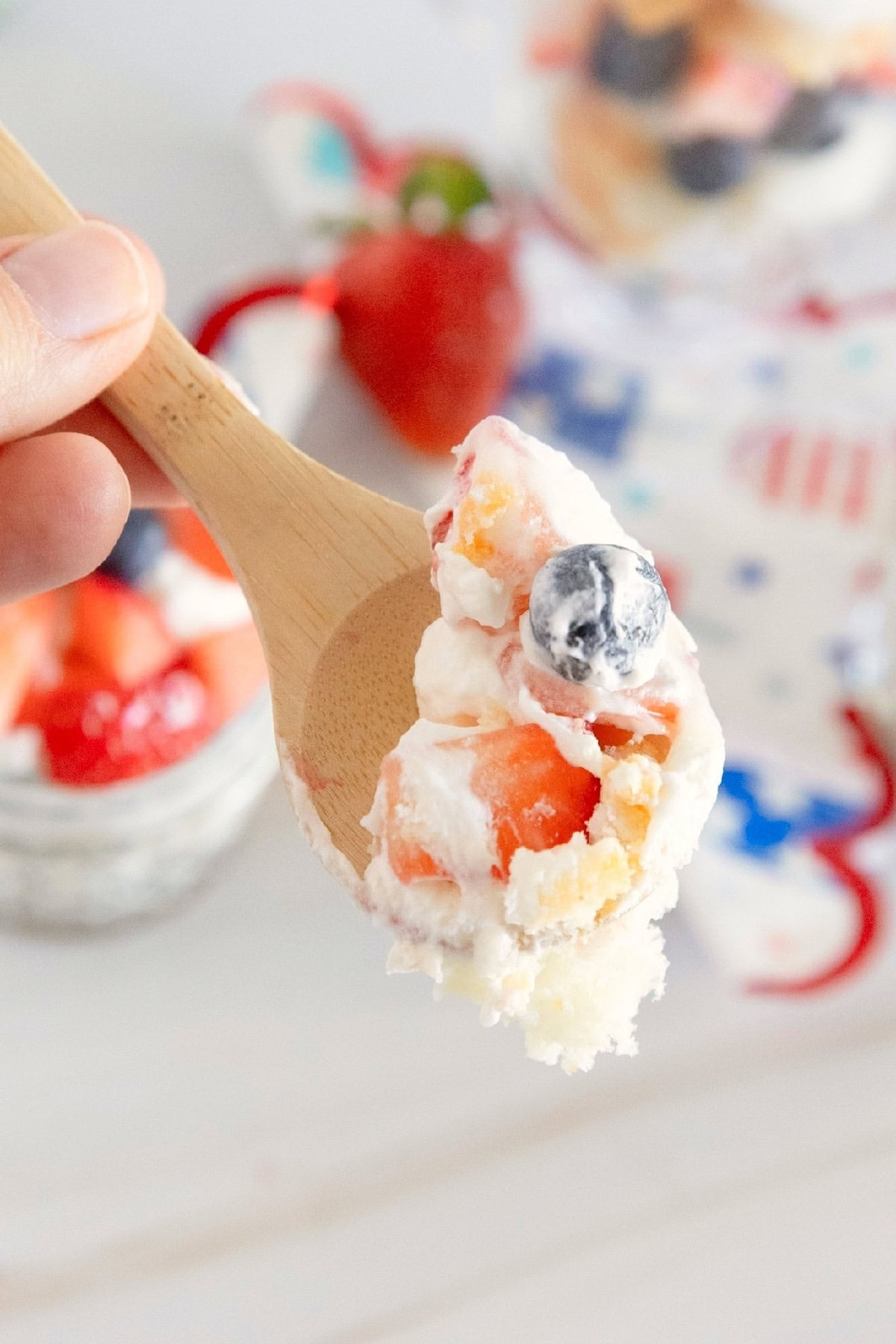 Spoonful of red, white, and blue trifle showing layers of cake, whipped topping, strawberries, and blueberries.