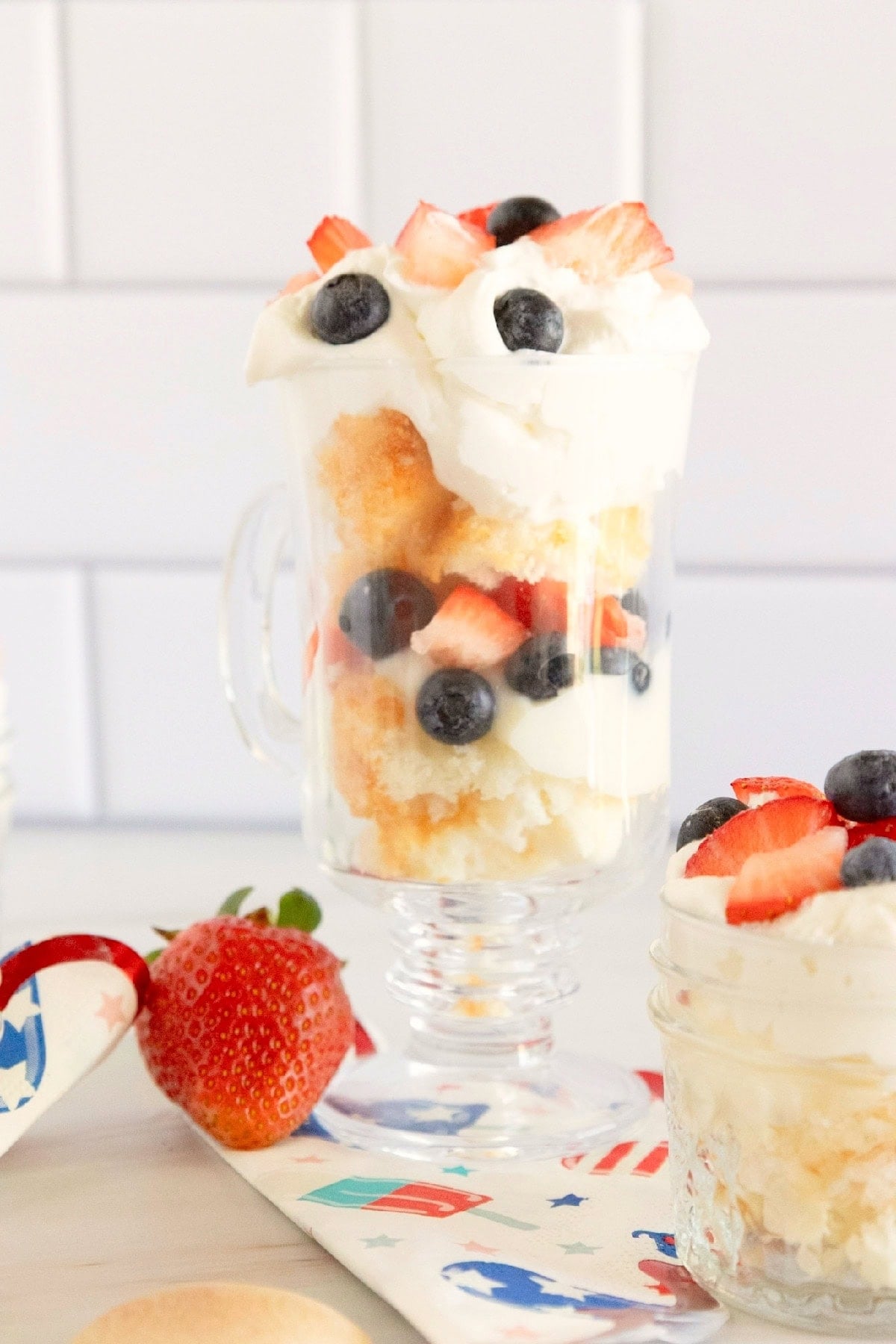 Bite of red, white, and blue trifle on a wooden spoon with strawberries, blueberries, whipped topping, and cake.