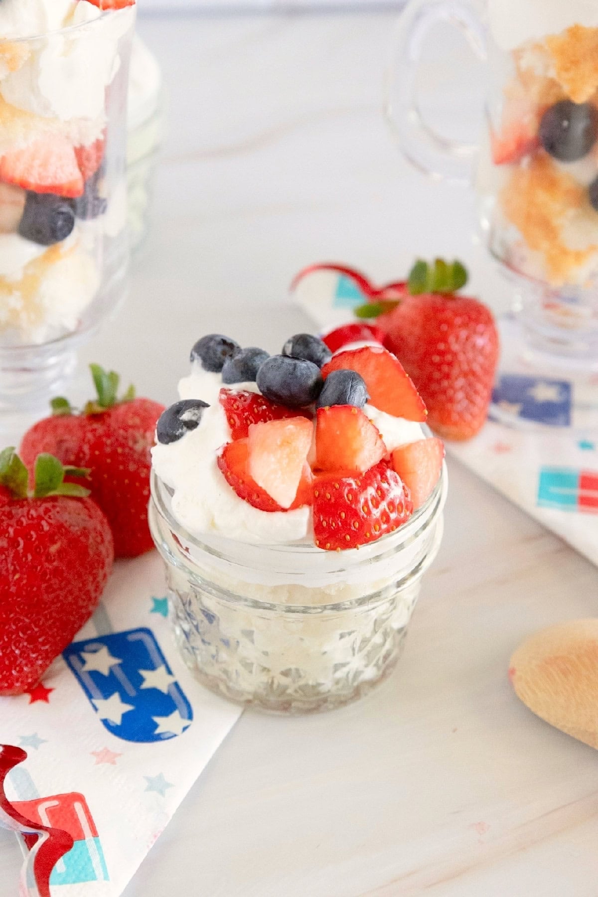 Close-up of a red, white, and blue trifle served in a glass mug with fresh strawberries and blueberries.