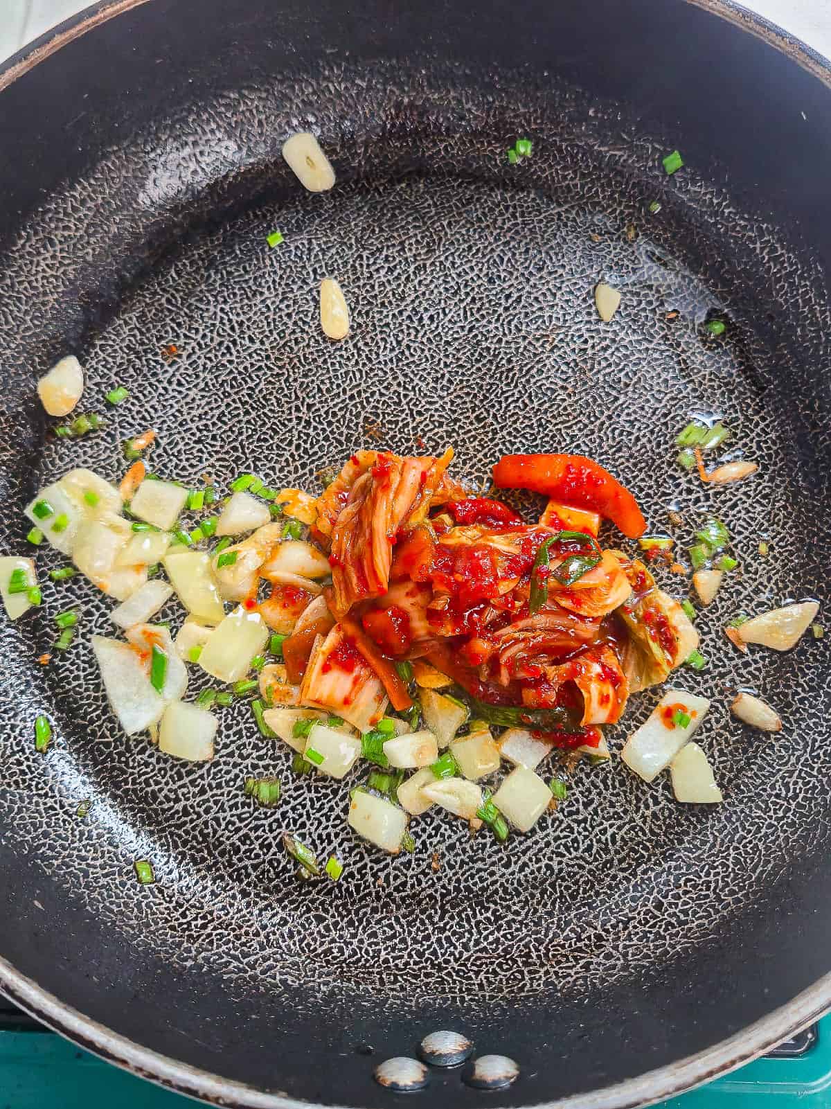 Garlic, diced onion, and green onions sautéing in a skillet for vegan kimchi fried rice.