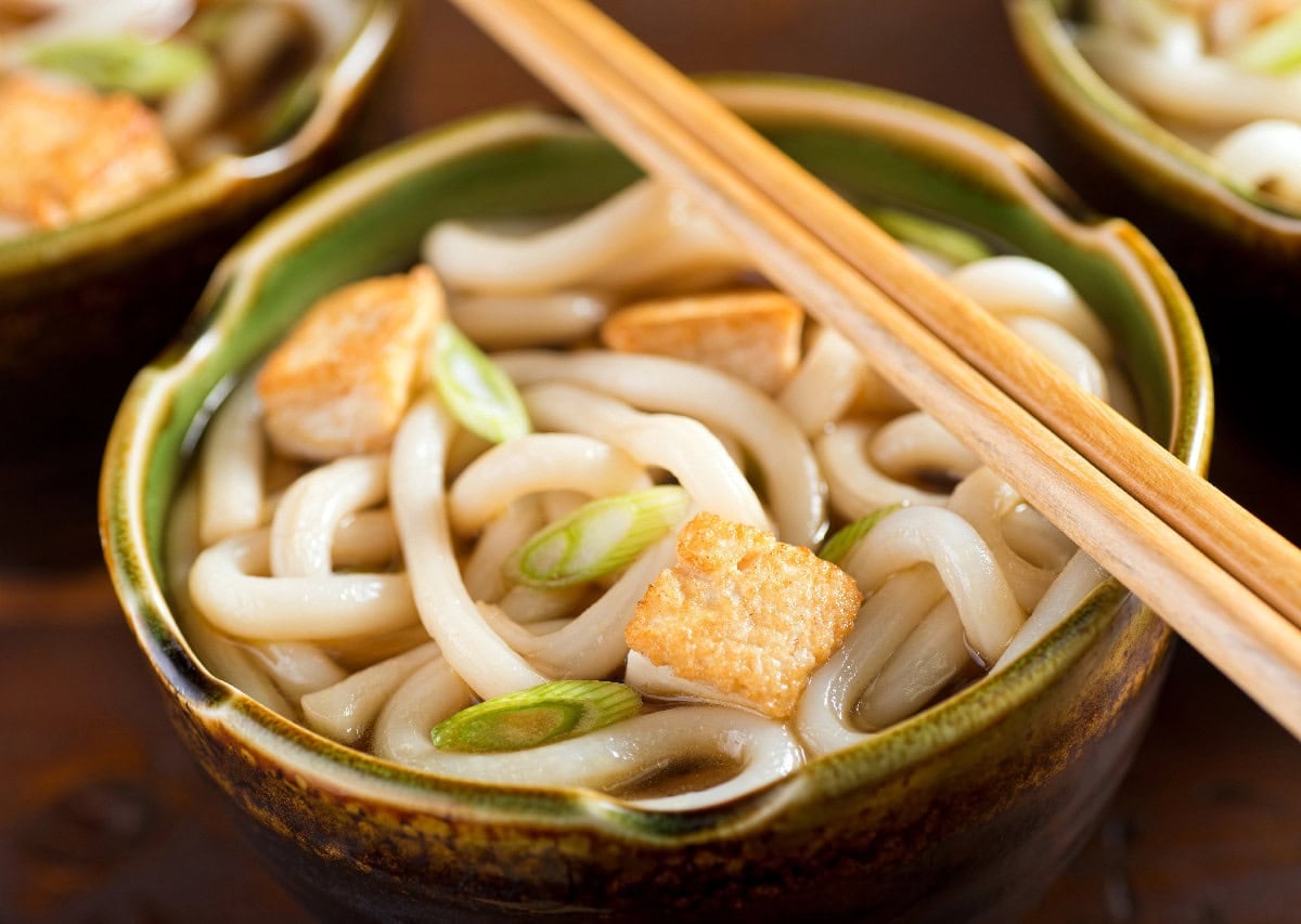 Japanese udon noodle soup with tofu, green onions, and chopsticks.
