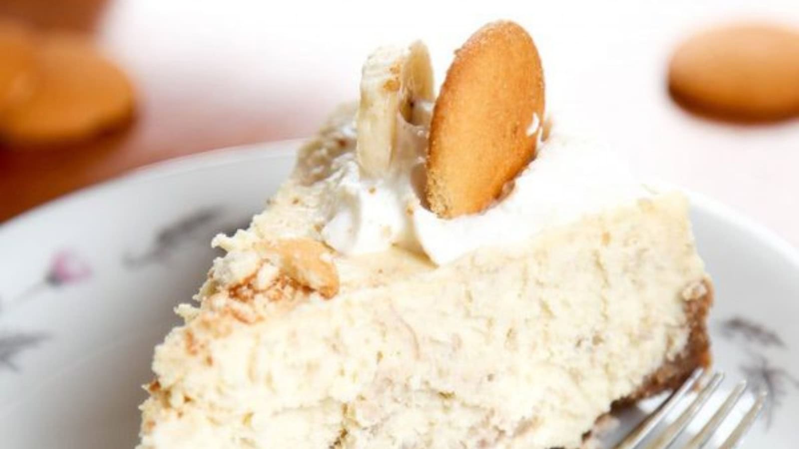 A slice of banana pudding cheesecake topped with whipped cream, vanilla wafers, and sliced bananas.