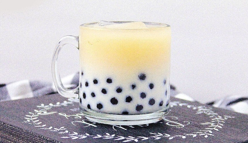 Iced milk tea with black tapioca pearls in a glass mug on wooden board.