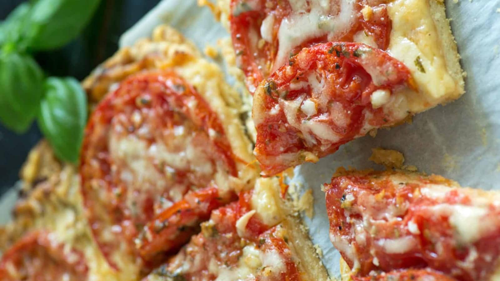 Savory tomato tart topped with fresh basil and flaky pastry.