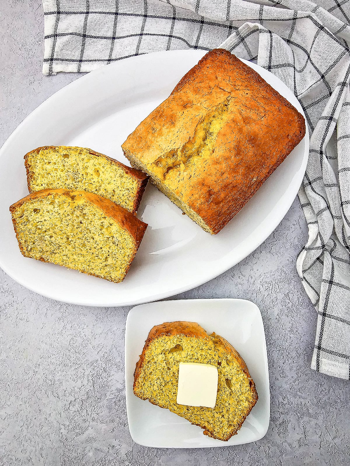 Freshly baked banana bread made with yellow cake mix served with sliced loaf and a buttered slice on white plates.