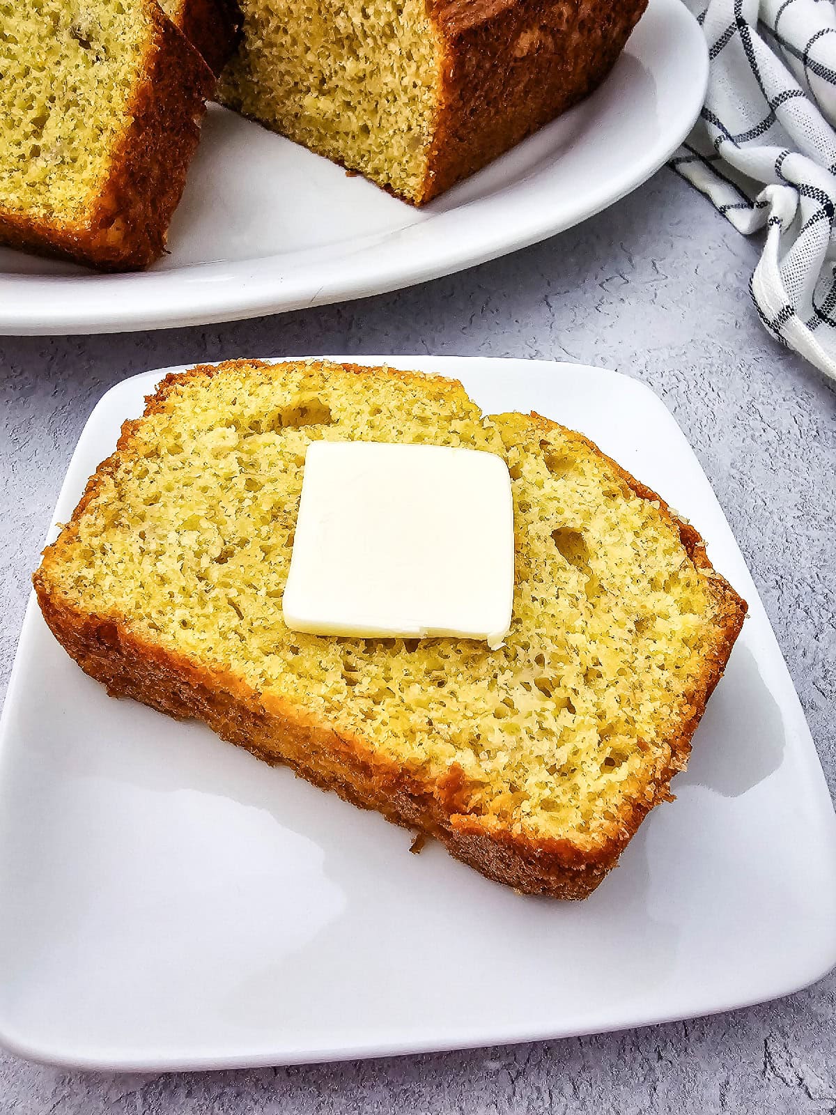Thick slice of banana bread made with yellow cake mix topped with a pat of butter on a white plate.