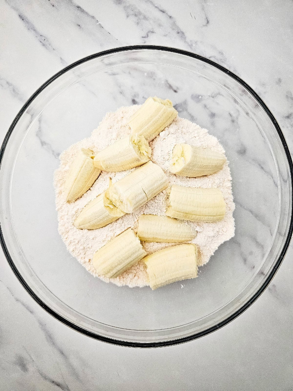 Yellow cake mix and ripe banana chunks added to a large mixing bowl before combining.