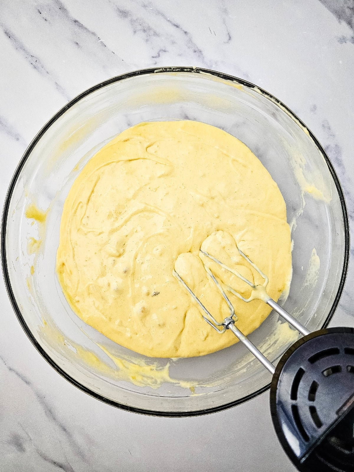 Banana bread batter mixed until smooth with an electric hand mixer in a glass bowl.
