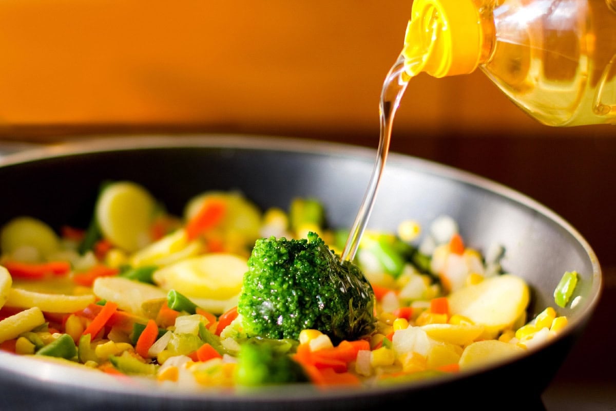 Pouring cooking oil into a pan of vegetables for a healthy stir fry.