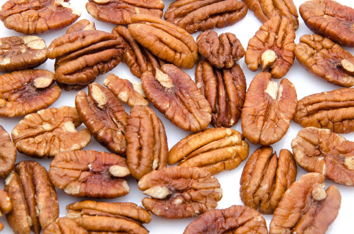 Raw pecan halves spread out on a white background before toasting.