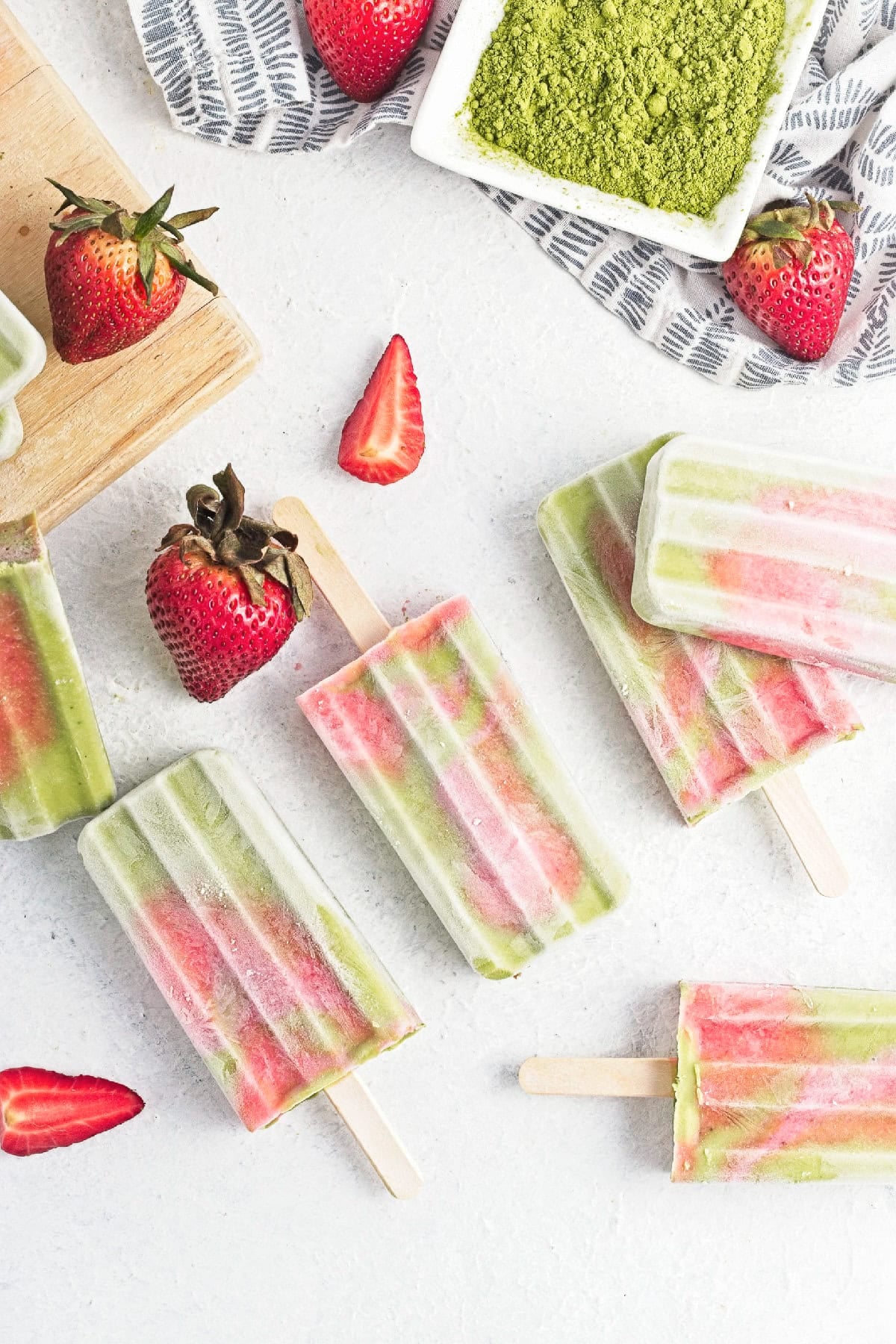 Overhead view of matcha strawberry popsicles arranged with fresh strawberries and matcha powder.