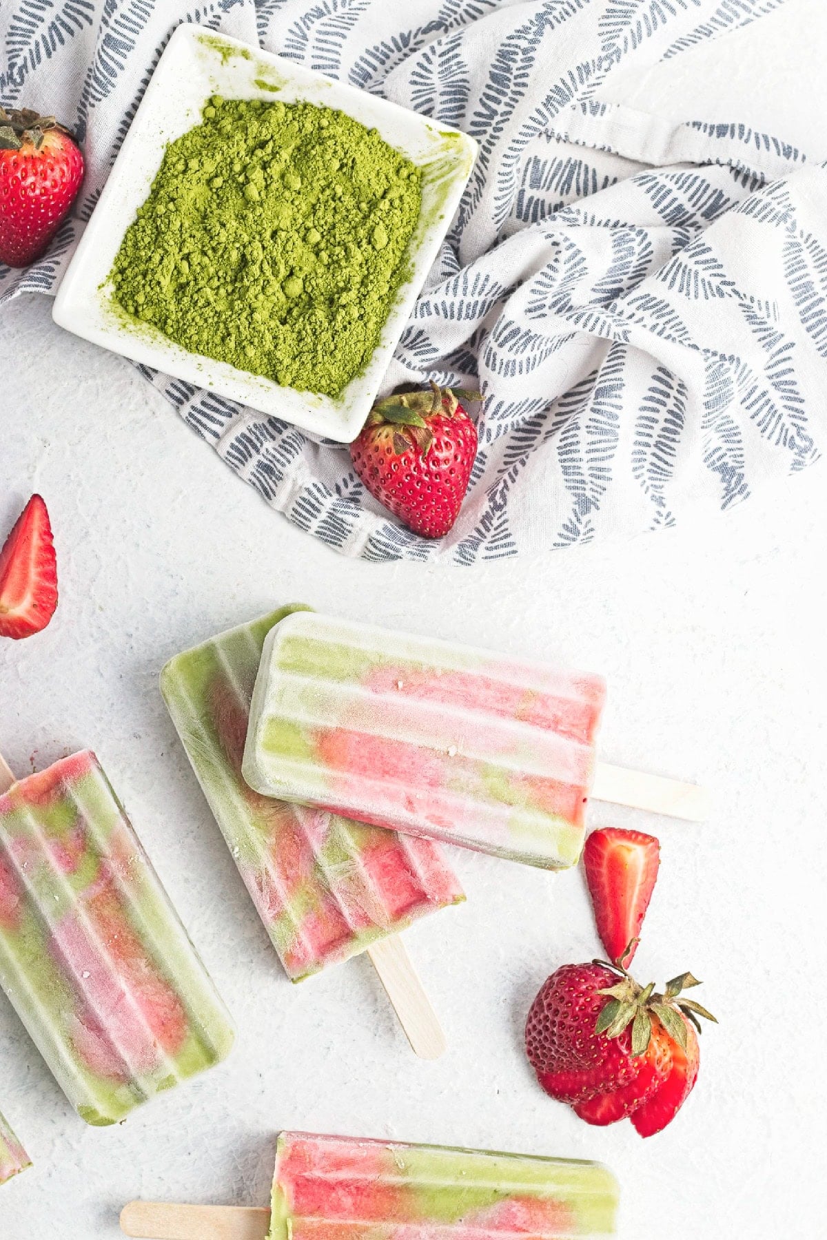 Matcha strawberry popsicles beside fresh strawberries and a dish of matcha powder.