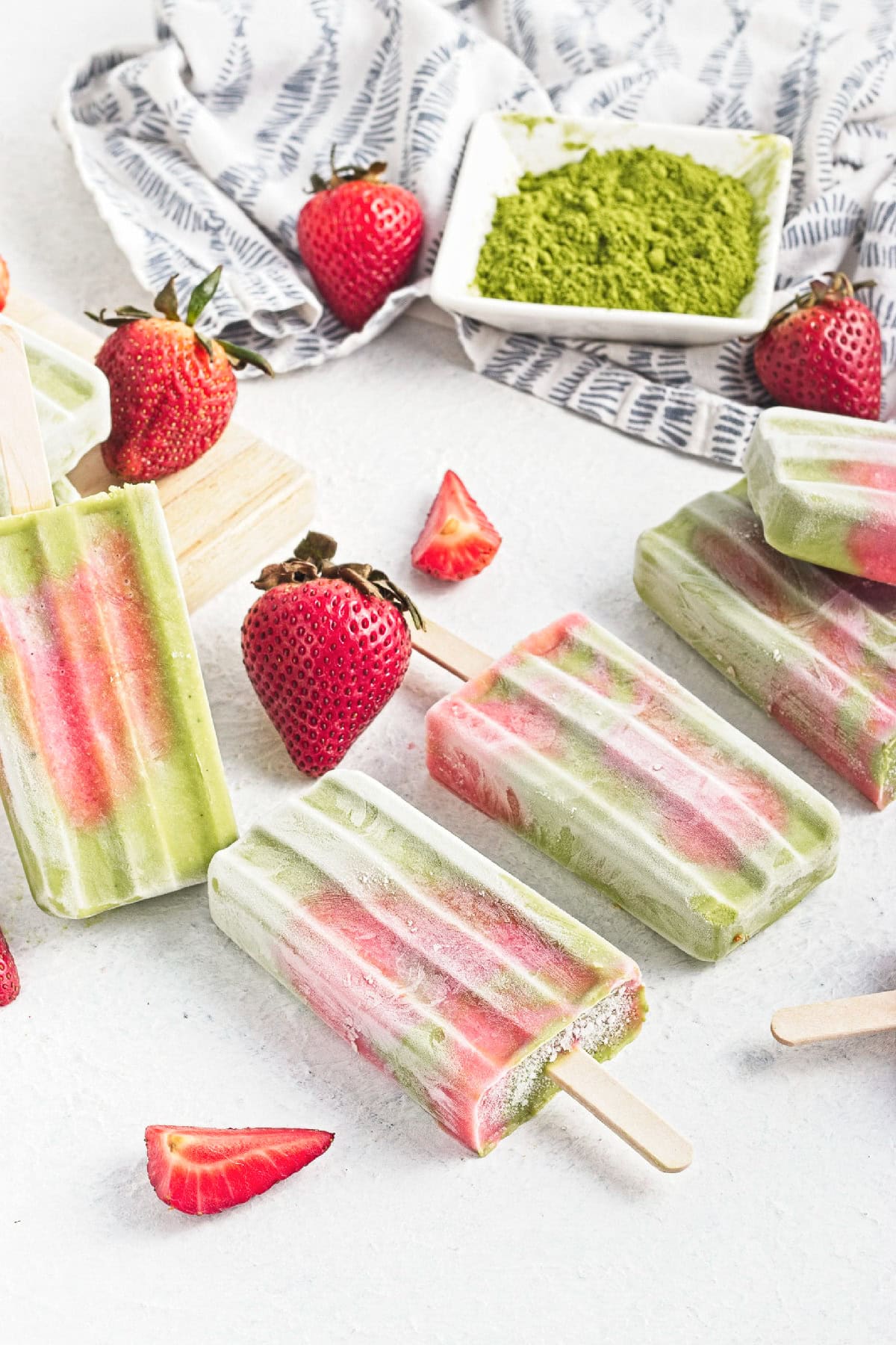 Homemade matcha strawberry popsicles arranged on a white surface with fresh strawberries.