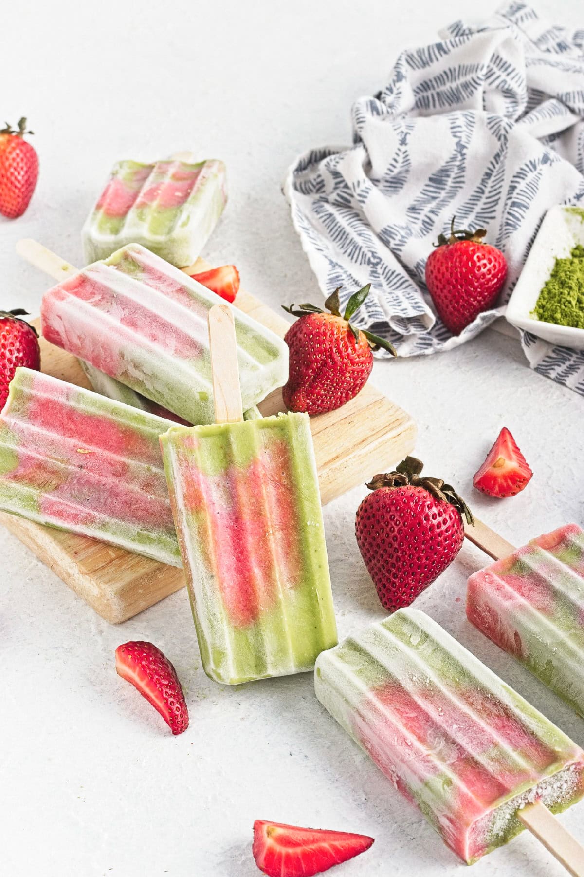 Matcha strawberry popsicles served on a wooden board with fresh strawberries and matcha powder.