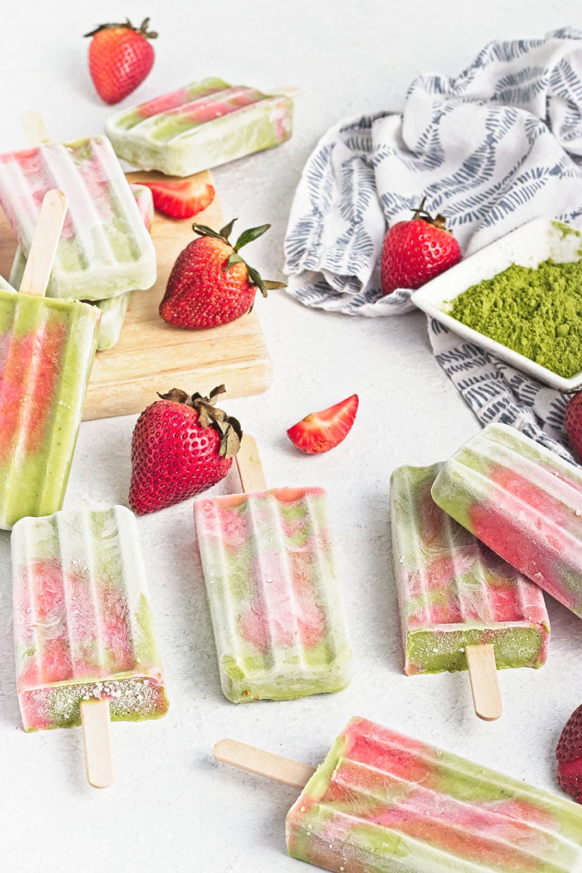 Assorted matcha strawberry popsicles arranged with fresh strawberries and a bowl of matcha powder.