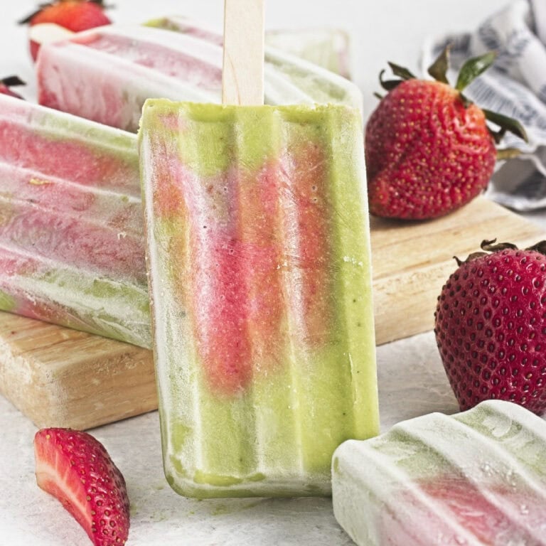 Matcha popsicles with strawberry layers standing upright alongside fresh strawberries and homemade popsicles.