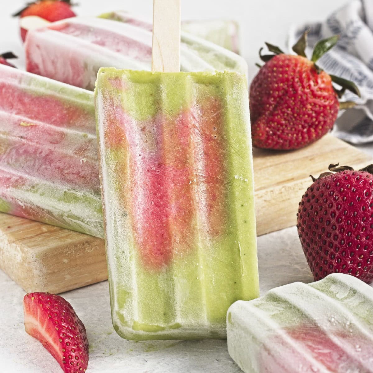 Matcha popsicles with strawberry layers standing upright alongside fresh strawberries and homemade popsicles.