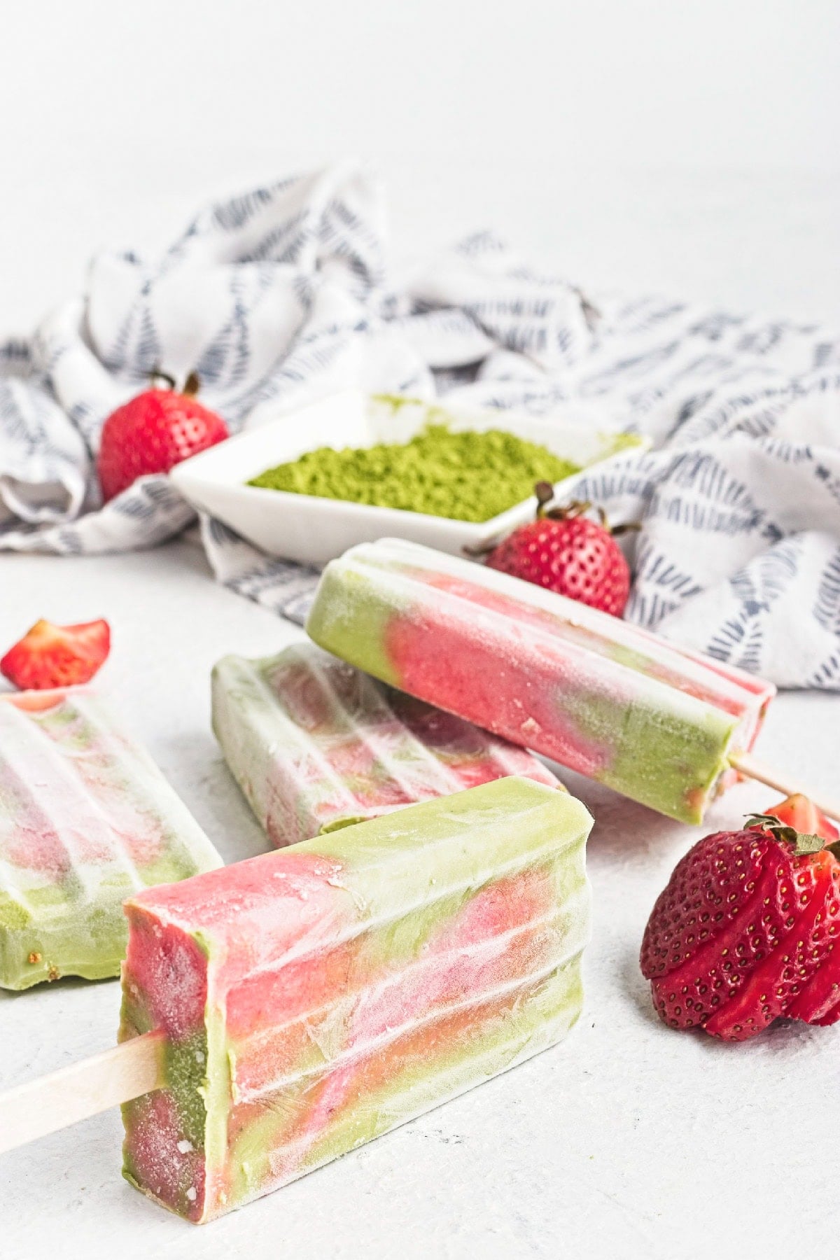 Side view of layered matcha strawberry popsicles with fresh strawberries and matcha powder.
