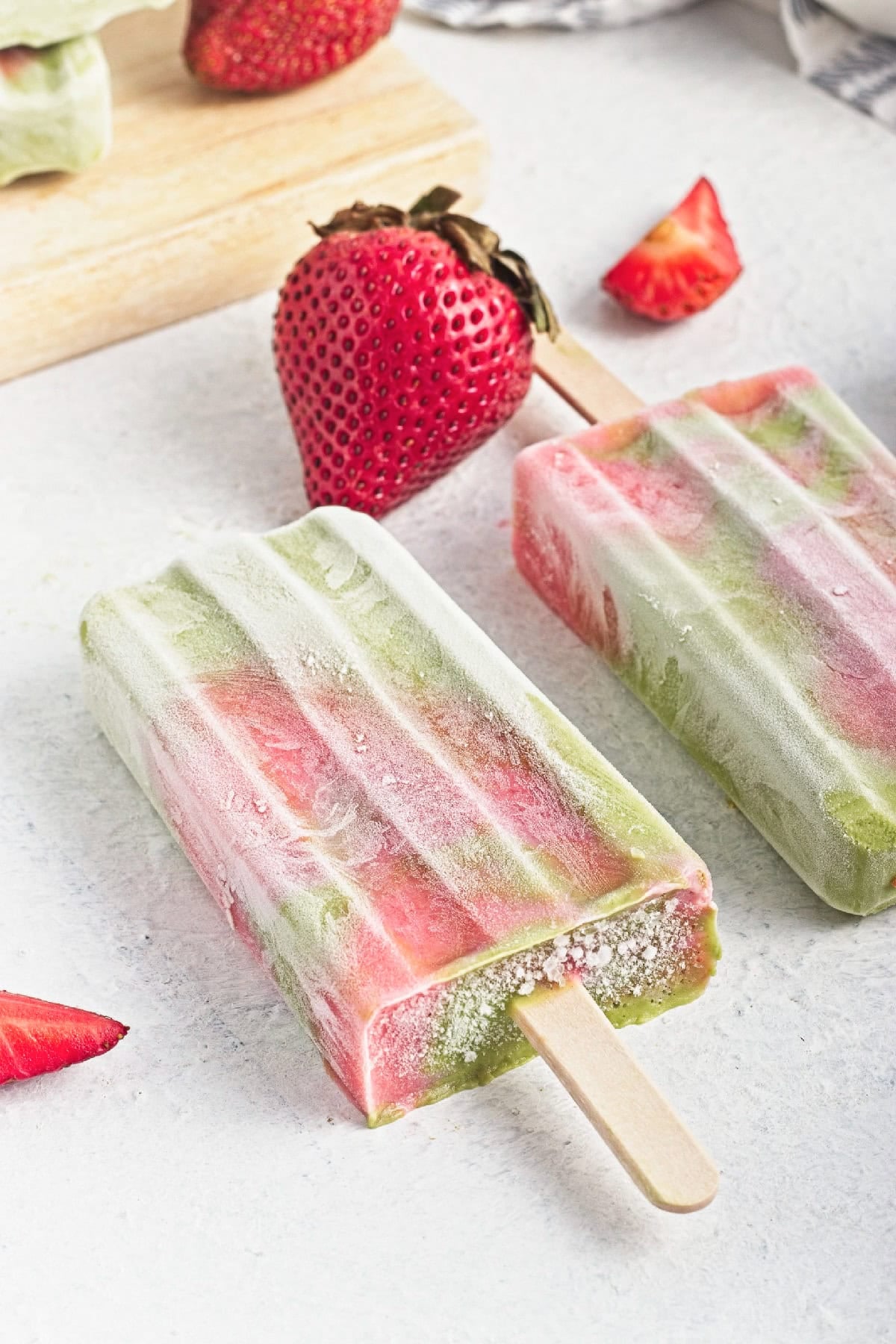 Close-up of a frosty matcha strawberry popsicle with fresh strawberries in the background.