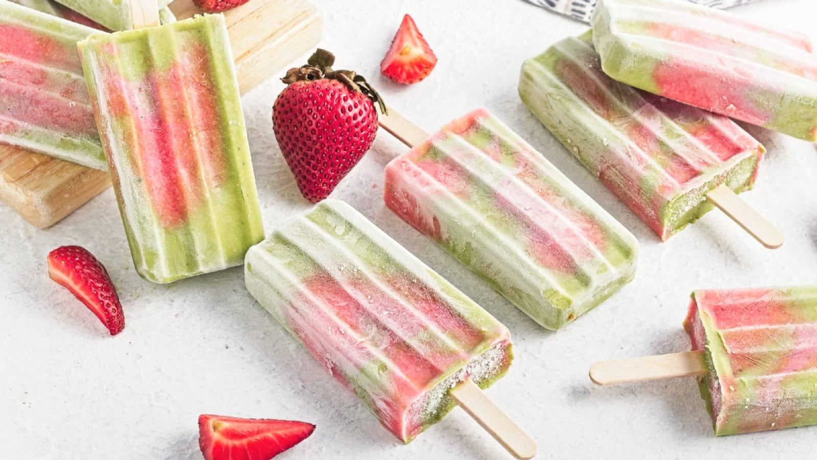 Homemade matcha strawberry popsicles arranged on a marble surface with fresh strawberries.