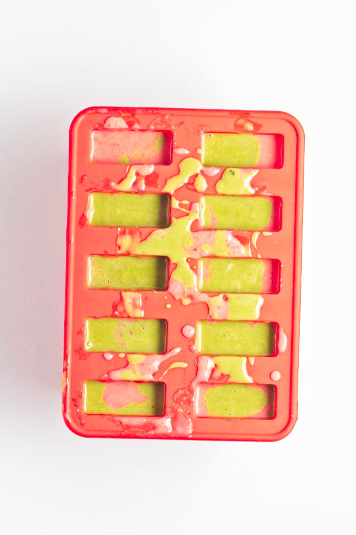 Strawberry and matcha mixtures poured into a popsicle mold to create layered popsicles.