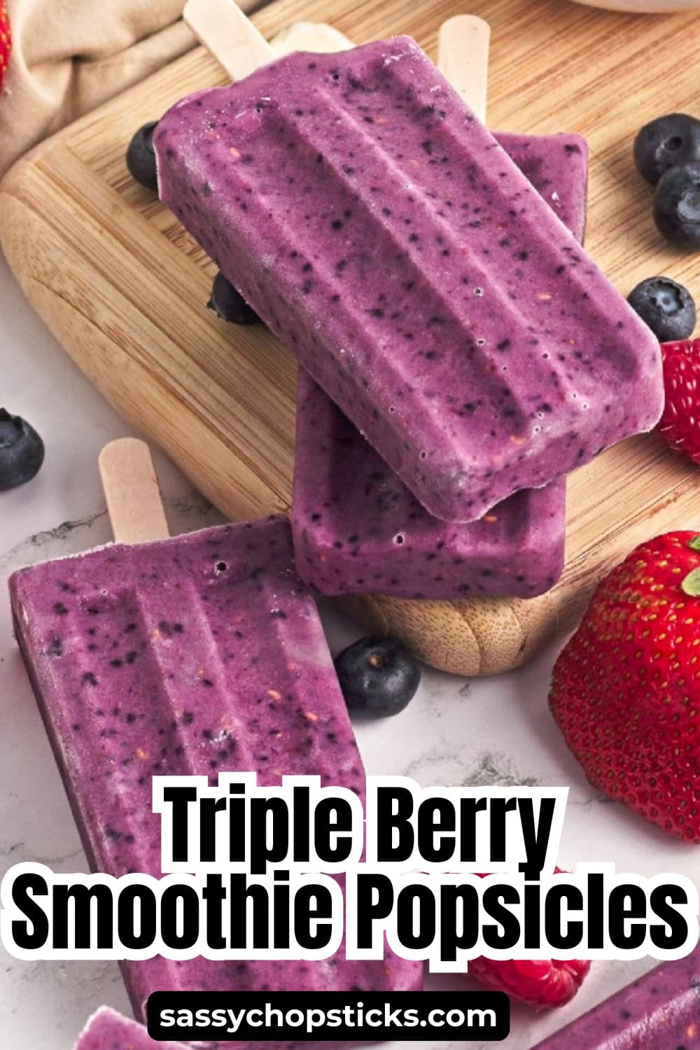 Triple berry smoothie popsicles stacked on a wooden board with fresh strawberries and blueberries, featuring the recipe title overlay.