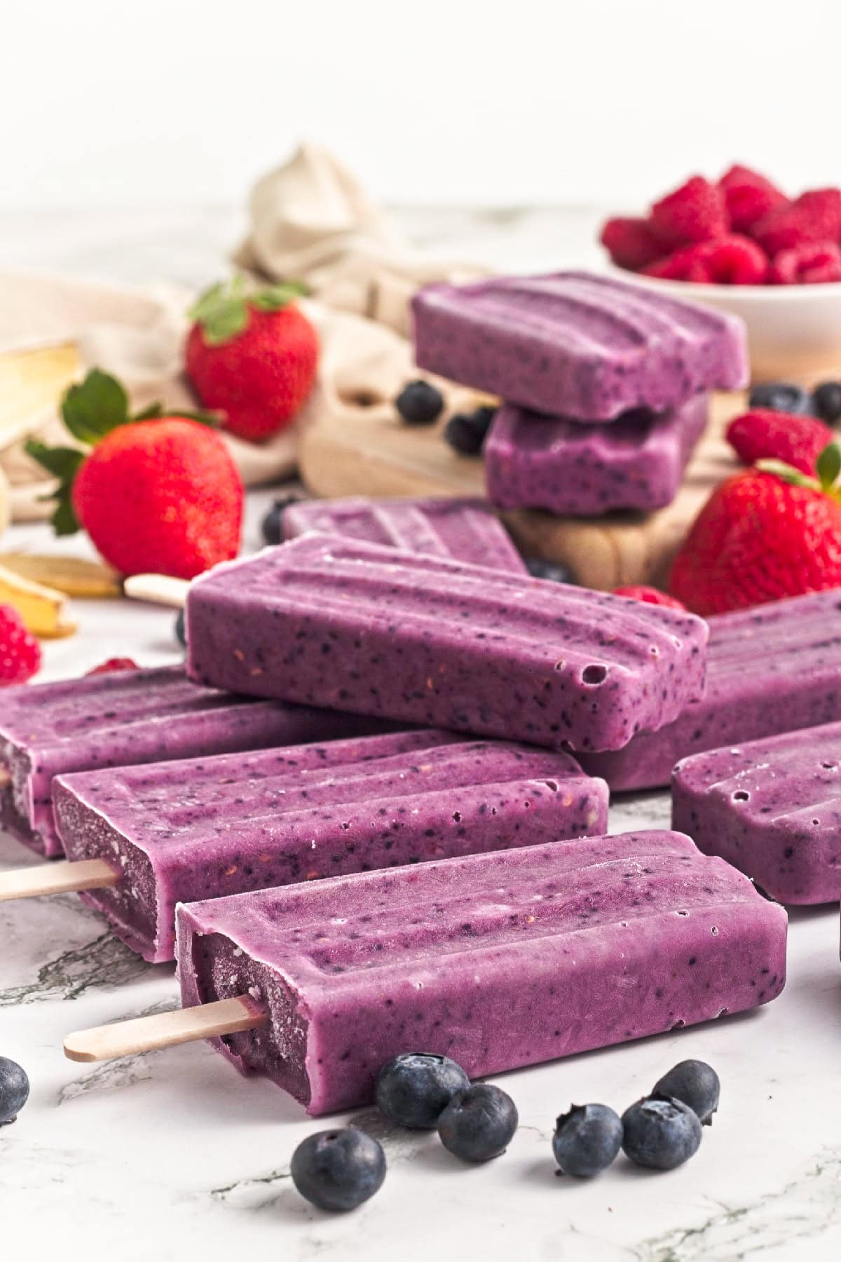 Close-up of homemade triple berry smoothie popsicles with fresh blueberries and strawberries on a marble surface.