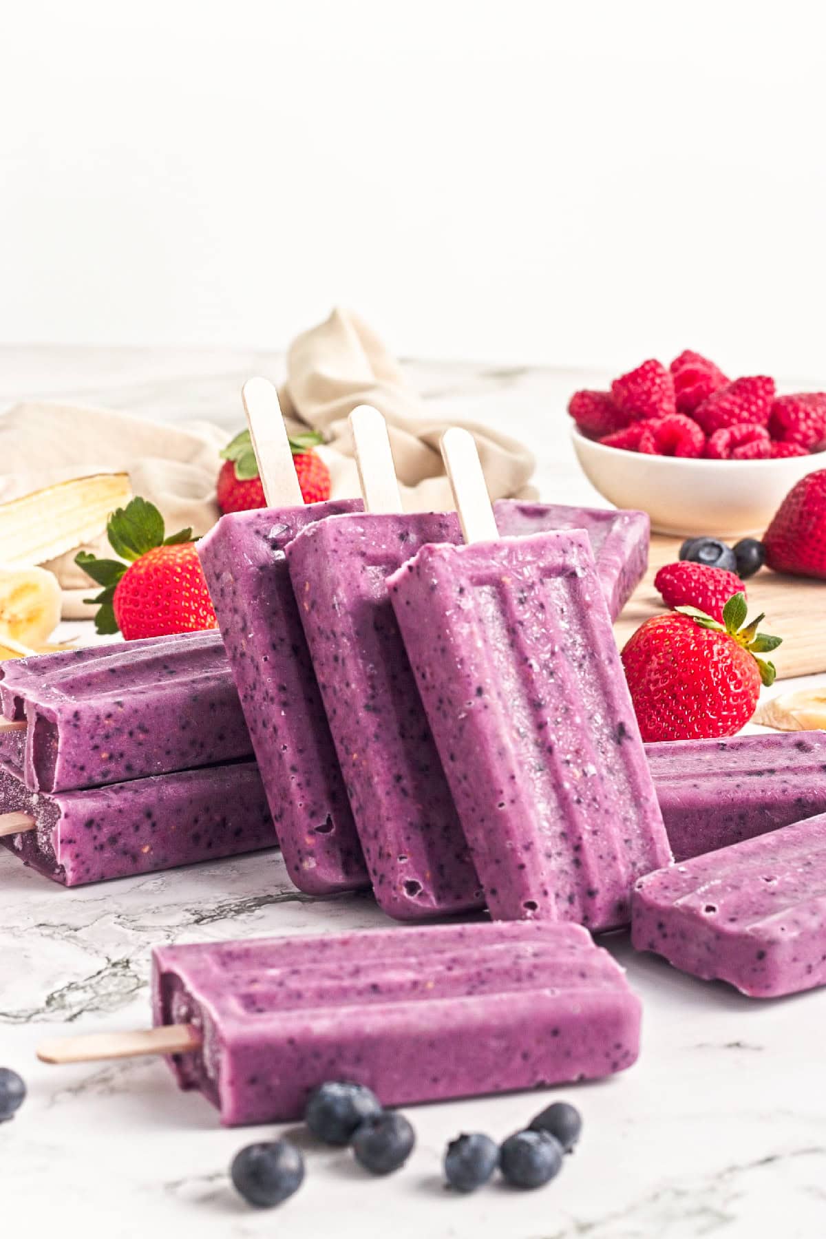Homemade triple berry smoothie popsicles standing upright with fresh strawberries, raspberries, and blueberries.