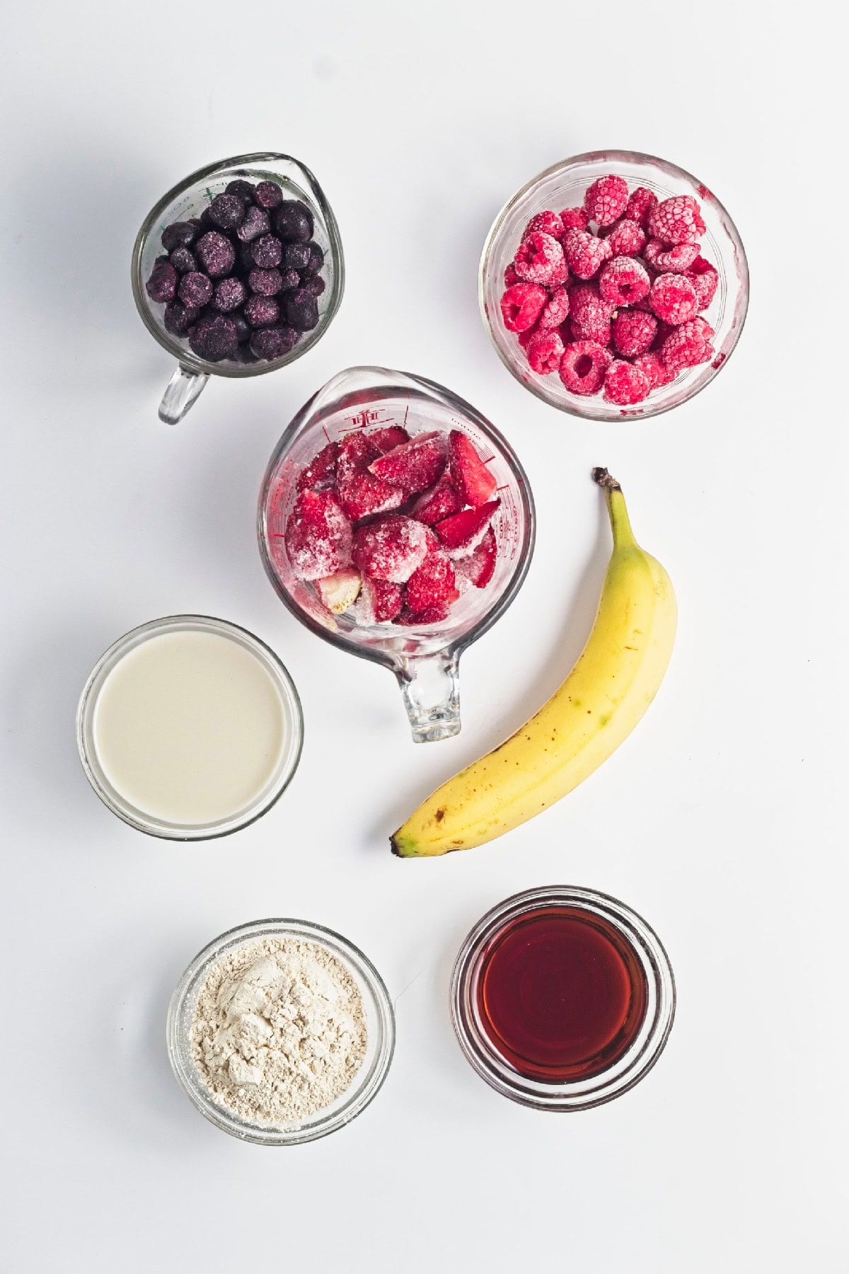 Ingredients for triple berry smoothie popsicles including frozen strawberries, blueberries, raspberries, banana, milk, vanilla protein powder, and maple syrup.