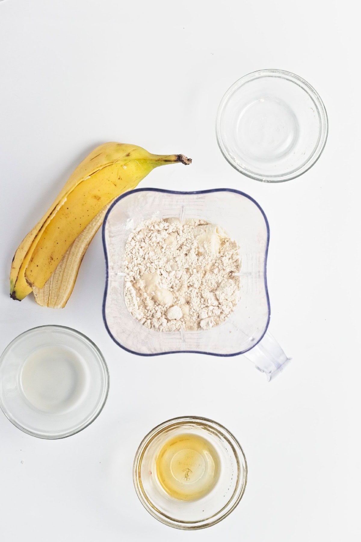 Banana, milk, vanilla protein powder, and maple syrup added to a blender for triple berry smoothie popsicles.