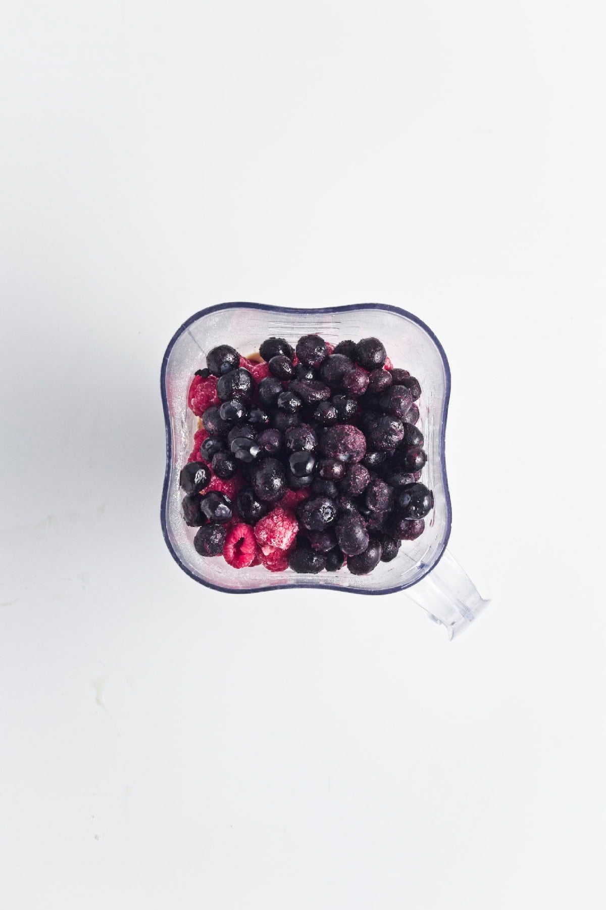 Blender filled with frozen blueberries and raspberries before blending into a smoothie.