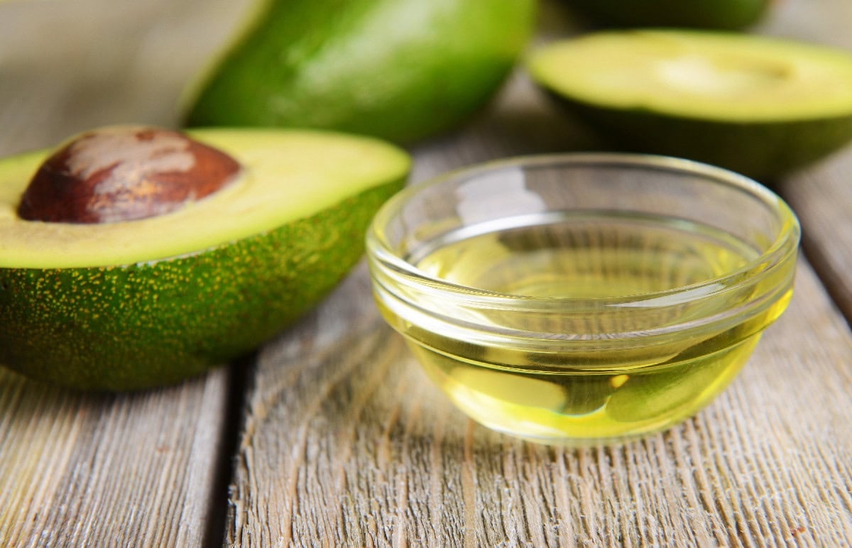 Avocado oil in a small glass bowl with fresh avocados, a mild substitute for sesame oil.