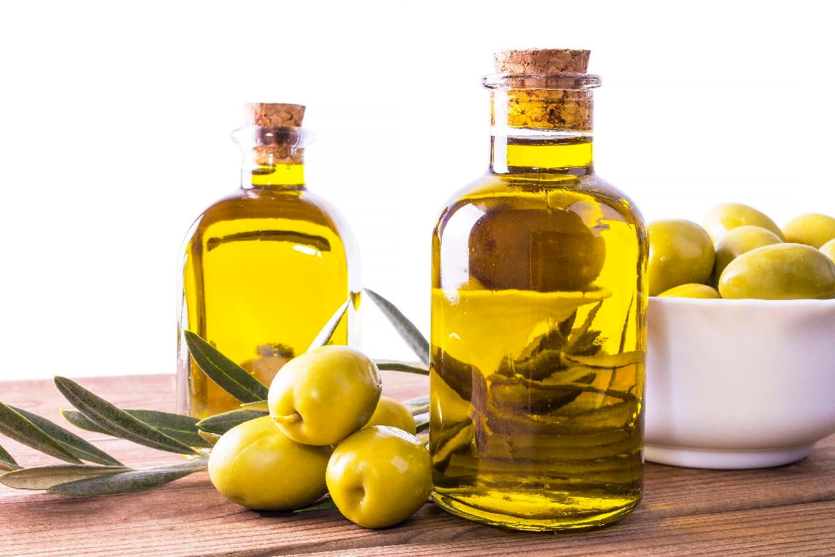 Extra virgin olive oil in glass bottles with fresh olives, a common sesame oil substitute.