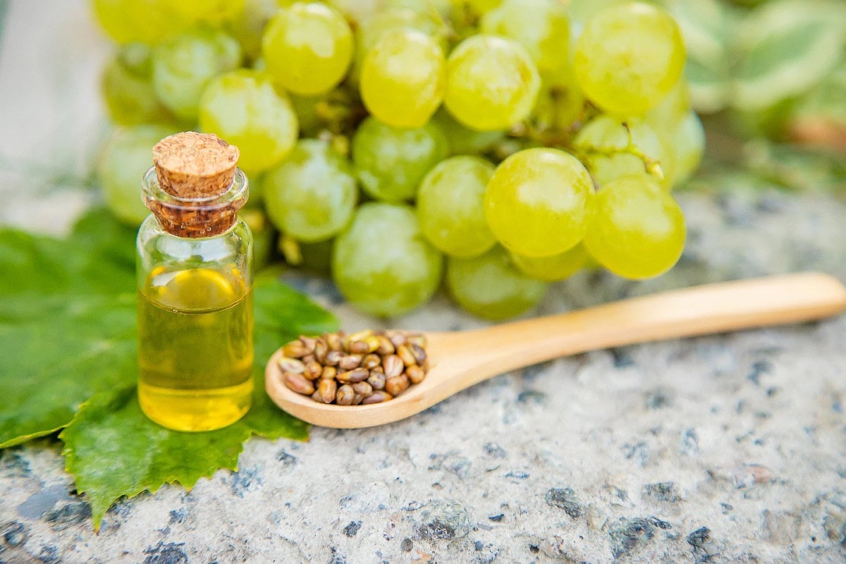 Grapeseed oil in a small bottle with fresh grapes and grape seeds, a neutral sesame oil alternative.
