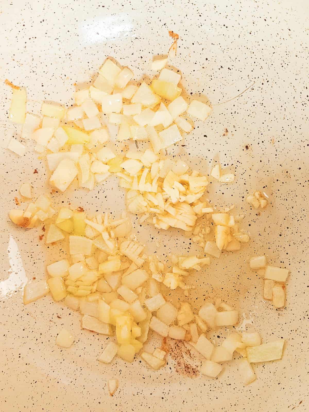 Chopped onion and garlic sautéing in a skillet for vegan nasi goreng.