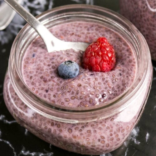 Berry chia pudding in a glass jar topped with a fresh raspberry and blueberry.