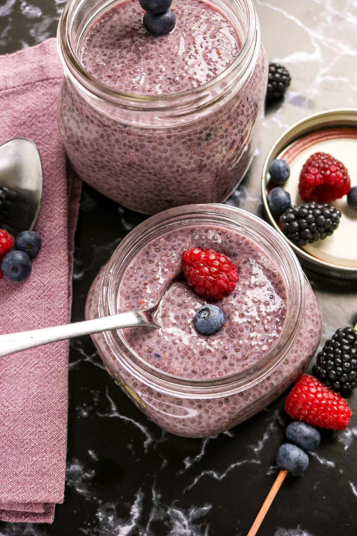 Two jars of berry chia pudding served with fresh raspberries, blueberries, and blackberries.