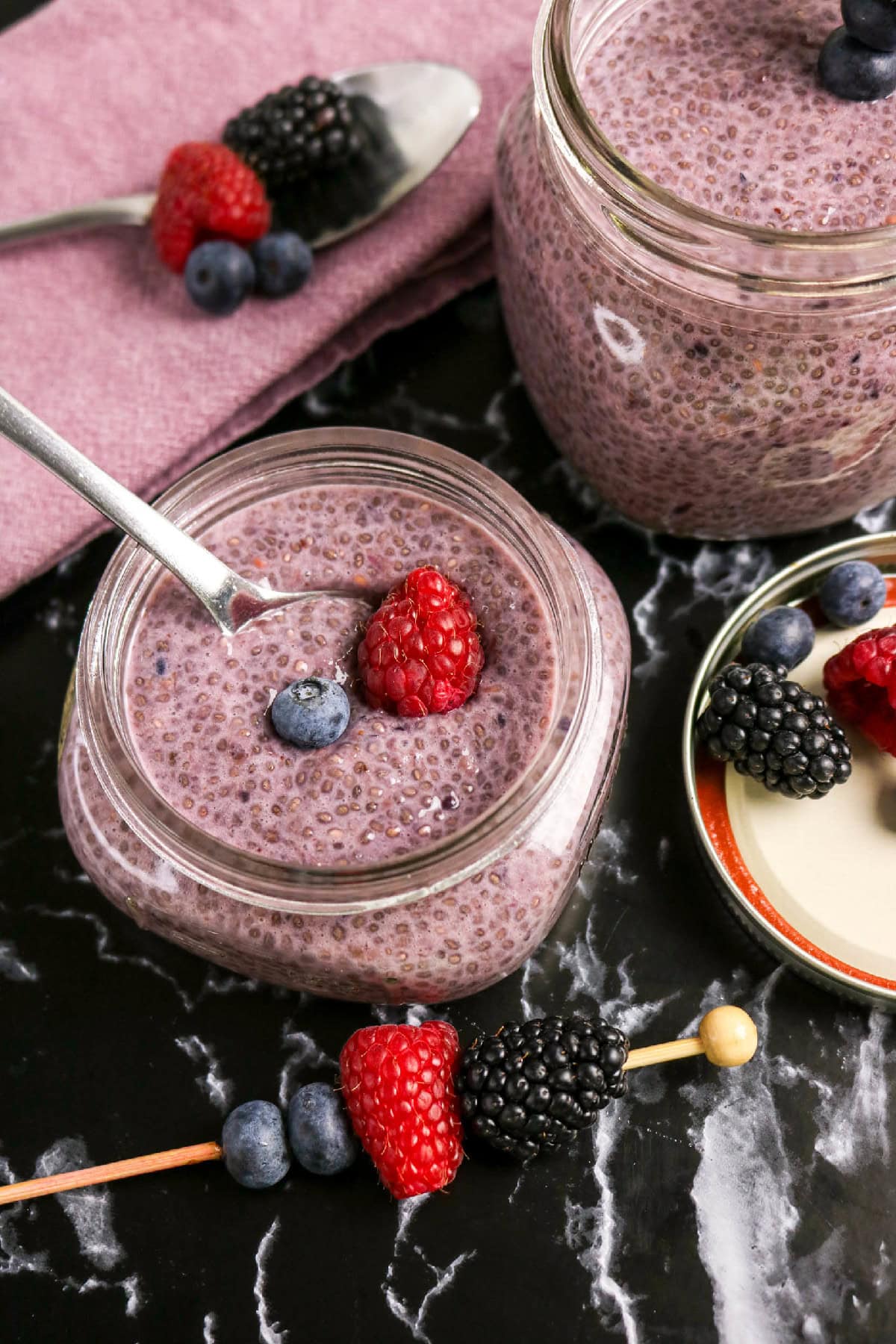 Berry chia pudding topped with a raspberry and blueberry and served with fresh mixed berries.
