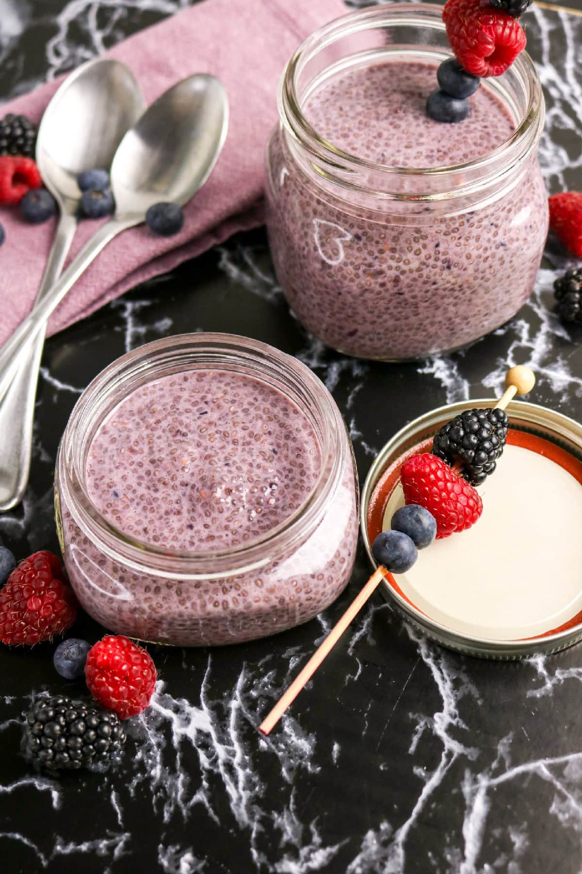 Two jars of berry chia pudding surrounded by raspberries, blueberries, and blackberries.