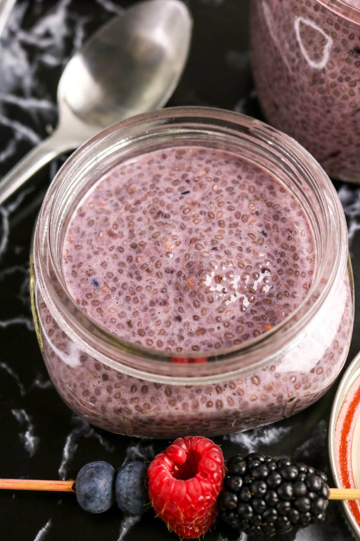 Close-up of creamy berry chia pudding in a glass jar with mixed berries in front.