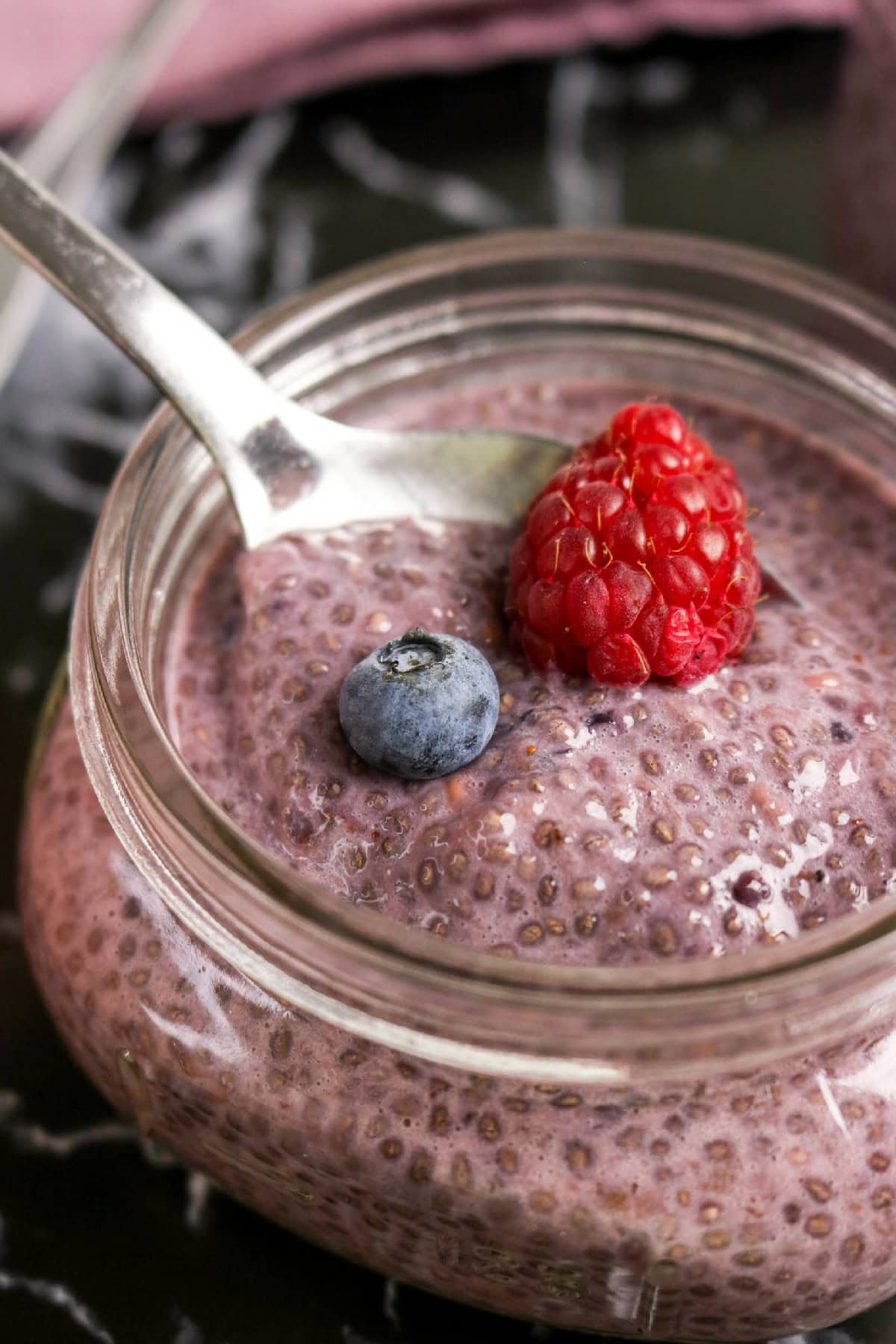 Close-up of berry chia pudding topped with a raspberry and blueberry beside a spoon.